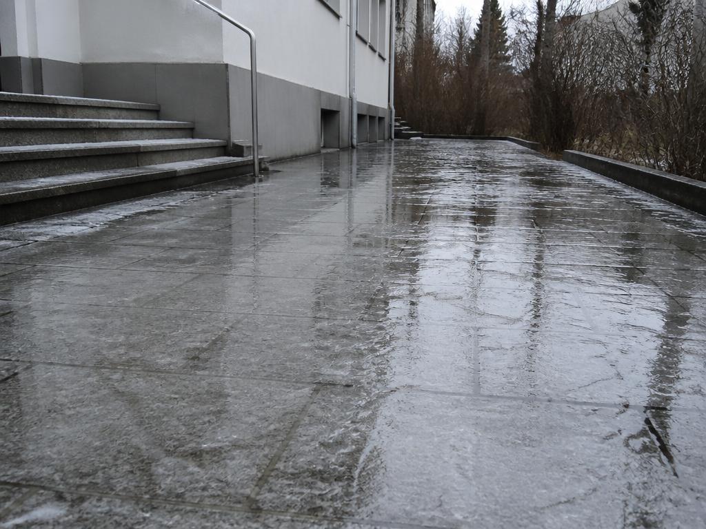 Vereister Gehweg mit dünner Eisschicht vor einem Hauseingang